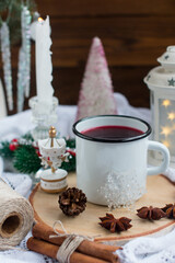 New Year's hot drink with spices on a white knitted blanket. Festive home decoration, Christmas trees and burning candles