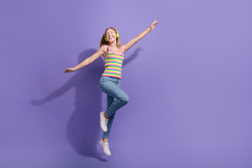 Fototapeta na wymiar Full length photo of lovely teen blonde lady jumping dance listen music wear trendy striped garment isolated on purple color background