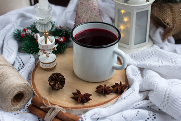 Fototapeta na wymiar New Year's hot drink with spices on a white knitted blanket. Festive home decoration, Christmas trees and burning candles