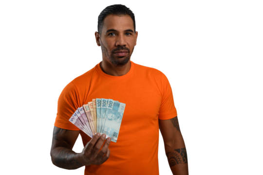 A man holding Brazilian money, wearing a basic orange T-shirt, looks at the camera
