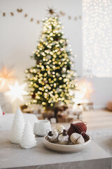 Christmas balls and decorations on table over defocused magic interior with christmas tree, stars and gifts at the background. Winter holiday, xmas home decor concept