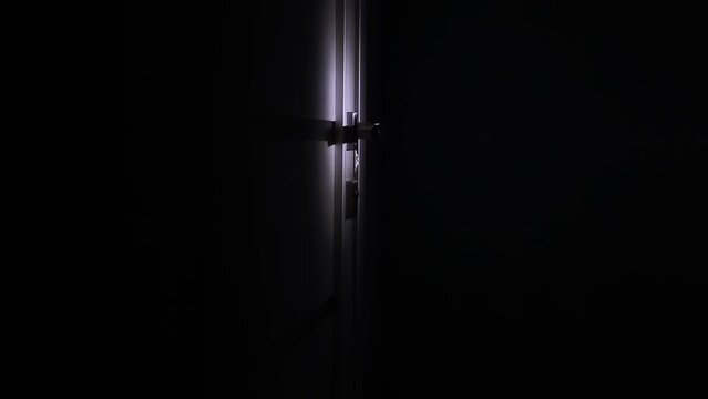 A man thief robs a house at night, shines a flashlight and opens the door. Night robbery, burglary. looped video. The criminal entered the house.