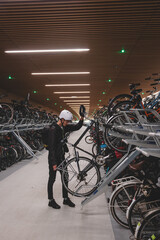 Traveller is surprised by the huge underground cycle station under the main overpass in Amsterdam, Netherlands. Inserting the wheel into the attachment and bike handle - obrazy, fototapety, plakaty