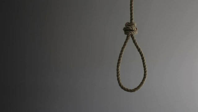 A suicide noose made of thick rope hangs against the background of a gray wall. Free space for text.