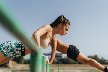 Fototapeta premium Caucasian couple of professional athletes doing pull ups on metal bars in a park. They exercise outdoors on a sunny day, showcasing their fit bodies and persistence in their training.