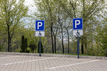 Two Disabled parking traffic signs fixed on poles. Road markings for parking spaces on the paving stones.