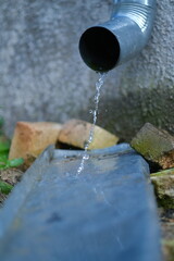 Rainwater flows from the water pipe. Blue tube. Bricks and a gray wall in the background.