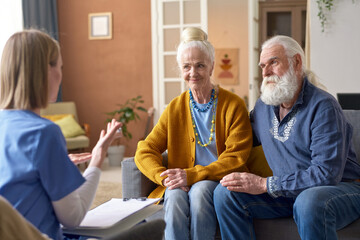 Senior couple sitting on sofa and talking to social worker during her visit to home