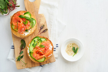 Open smoked salmon sandwiches with cream cheese, cucumber, sesame seeds, microgreens, spinach, and peas leaves on light old wooden background. Healthy breakfast food. Delicious snack. Top view.