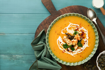 Pumpkin and carrot cream soup with herbs, seasonings and seeds in bowl on dark wooden background in rustic style. Thanksgiving traditional autumn pumpkin cream soup. Top view.