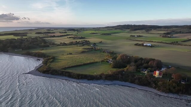 Aerial footage of the Isel M&oslash;n seascape landscape featuring the emerging M&oslash;n lighthouse, distinguished by its striking yellow tower, white gallery, and vibrant red-roofed lantern.