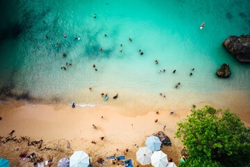 Aerial view of a paradise-like bustling beach with white sand and turquoise-colored waves lapping up