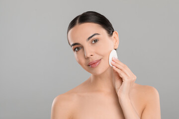 Beautiful woman removing makeup with cotton pad on light grey background, space for text