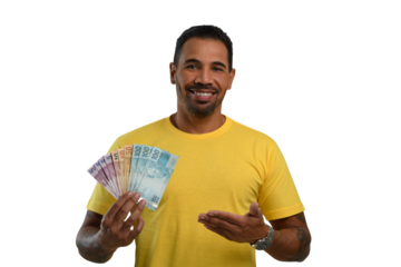 a smiling man points to the Brazilian money in his hand, wearing a yellow T-shirt against
