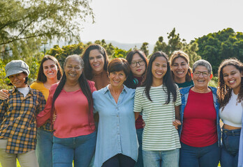 Group of multi generational women hugging each other while smiling on camera at city park - Multiracial female friends and community concept - obrazy, fototapety, plakaty
