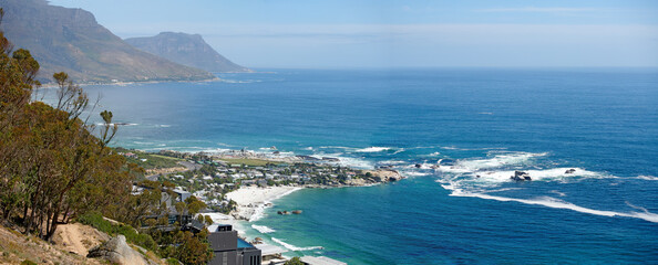 Panorama of a mountain coastline with quiet ocean against a blue sky in South Africa from above. Scenic wallpaper of a serene landscape of calm waves near Camps Bay with a peaceful sea view.