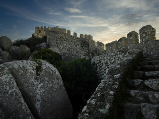 Medieval Castelo dos Mouros aka Castle of the Moors in Sintra, Portugal. Watchtower and defensive wall climbing the ridge of the mountain by sunset