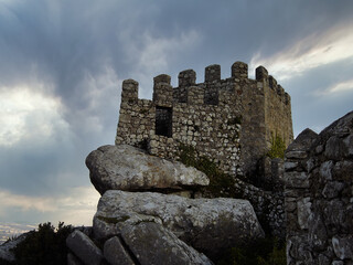Watchtower and defensive wall in the Medieval Castelo dos Mouros aka Castle of the Moors in Sintra, Portugal. Dusk and storm overcast sky