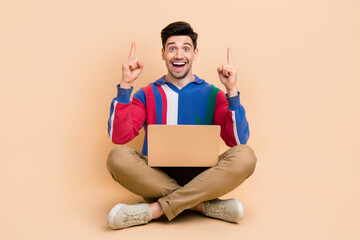 Full length photo of surprised funny guy indicating fingers up above head recommend app for laptop isolated on beige color background