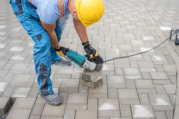 Laying interlocking paving. A worker sawing the paving stone with an angle grinder.