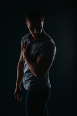 Naklejka premium Appealing and well-built man standing in a dark room and flexing his muscles