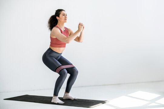 Young sporty fit woman in sportswear squats with fitness elastic band on legs