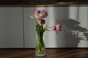 Close-up image of a vase filled with vibrant pink tulips arranged against a white countertop