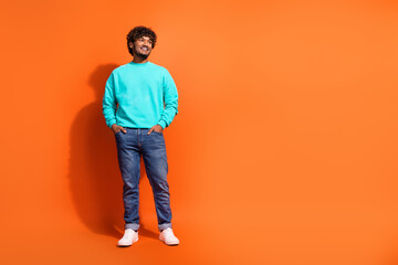 Fototapeta premium Full body portrait of cheerful creative person put arms pockets look empty space isolated on orange color background