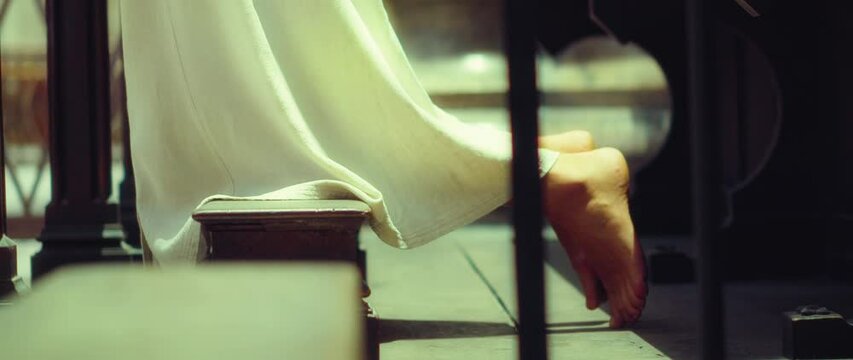 Barefoot girl in a long dress praying on her knees in church. Close-up of feet.