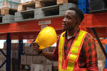 African worker waving hard hat to relieve heat during break time at warehouse, working in hot and...