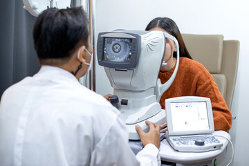 Male ophthalmologist checking vision of young female patient in clinic with auto refractometer
