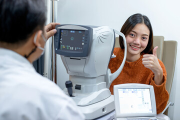 Male ophthalmologist checking vision of young female patient in clinic with auto refractometer,...