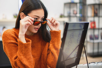 Beautiful girl choosing a glasses in optician store, Asian girl wearing a sweater testing out her...