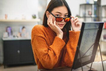 Beautiful girl choosing a glasses in optician store, Asian girl wearing a sweater testing out her eyeglasses selection