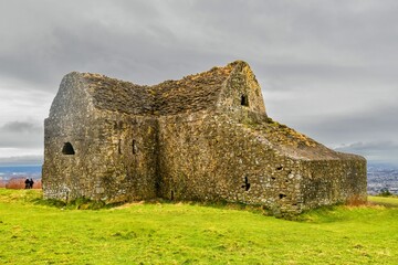 Traditional stone building situated atop a lush green meadow, with a gloomy sky in the background