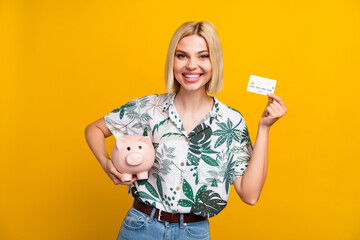 Photo portrait of attractive young woman hold credit card pig dressed stylish leaves print clothes isolated on yellow color background