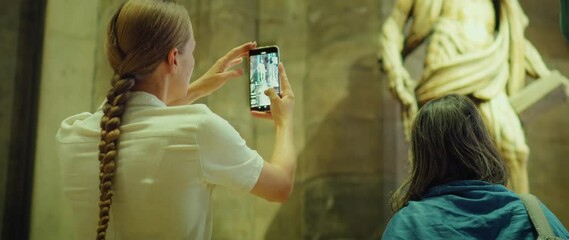 Crowd of tourists visits the museum. Woman at an exhibition of historical sculptures takes pictures on phone