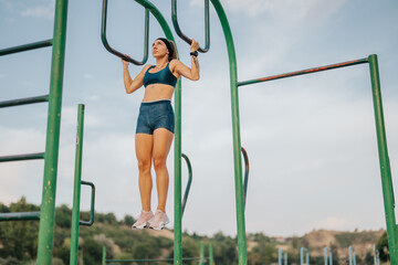 Fototapeta premium Fit girl warming up outdoors, stretching and flexing on metal bars. Athletic body inspire a healthy and active lifestyle. Sporty woman showcasing strength and flexibility before training.