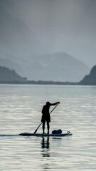 Adult male paddling a surfboard on a large body of water with a scenic mountain backdrop