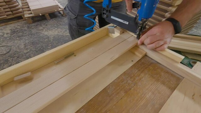 Craftsman in a carpentry workshop hammers nails with a pneumatic hammer. Making a stool