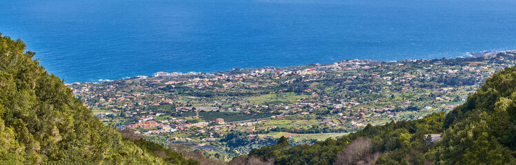 Fototapeta na wymiar Landscape of a coastal city between hills and mountains from above. A peaceful village beside calm blue ocean water in the Canary Islands. High angle view of Los Llanos, La Palma in summer