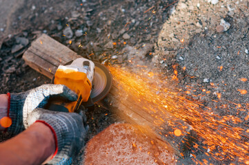 Bright sparks of metal fly from the disk of an angle grinder. A power tool in the hands of a worker is used to cut metal parts.