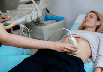 Unrecognizable doctor using ultrasound and screening woman's stomach. Pregnant woman getting...