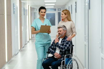 Obraz premium Smiling young female nurse with grey haired man in wheelchair with her beautiful wife at rehab center.