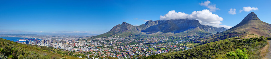 Naklejka premium Panoramic scene of Cape Town, South Africa. Table Mountain, Lions Head and Signal Hill against a blue sky background, overlooking the city. Aerial view of the urban and natural environments