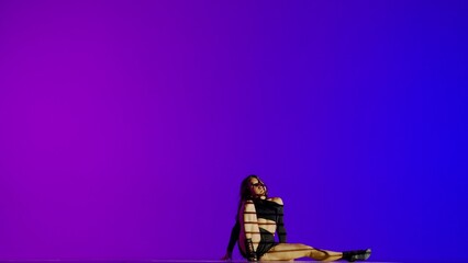 Attractive woman dancing heels dance in a studio. Blue to purple neon gradient background, striped falling shadow. Black sexy costume, high heels. Modern sensual choreography. Full length.