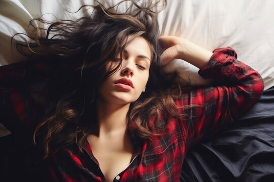 Young woman in black and red man's shirt lounging on bed.