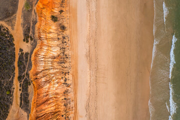 Algarve, Portugal coastline with sandy beach,  Atlantic Ocean waves and red cliffs at sunset. Aerial drone view.