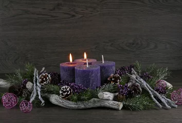 Fototapeten Adventsdekoration: Adventskranz mit zwei lila brennenden Kerzen für den zweiten Advent mit Tannenzweigen und Weihnachtsdeko vor einer Holzwand mit Platz für Text. © Racamani