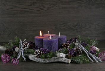 Adventsdekoration: Adventskranz mit einer lila brennenden Kerzen für den ersten Advent mit Tannenzweigen und Weihnachtsdeko vor einer Holzwand mit Platz für Text.